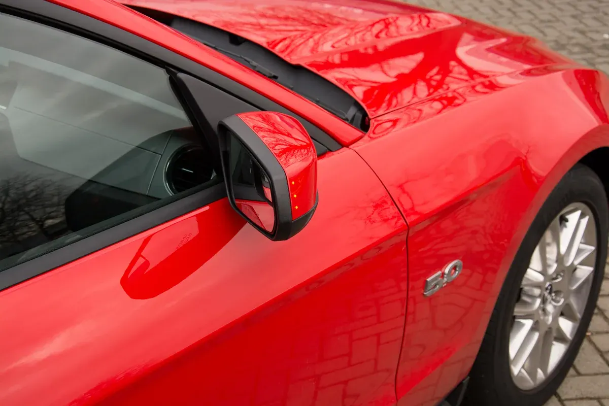 Three amber side indicator lights illuminated in a red Mustang wing mirror